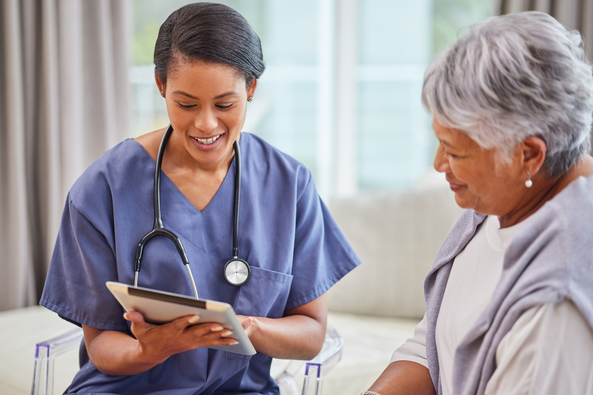 A nurse shows an older woman information on an iPad at an at-home visit. 