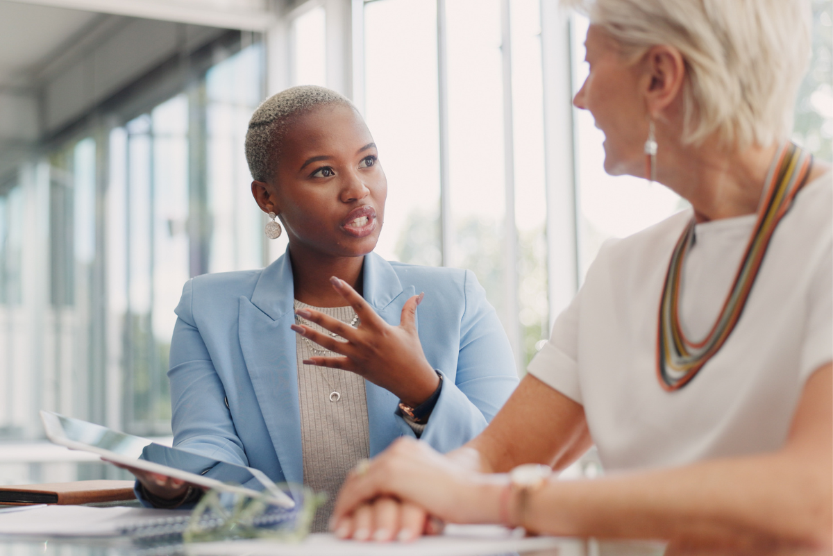 Two business women talking in a large glass conference room.