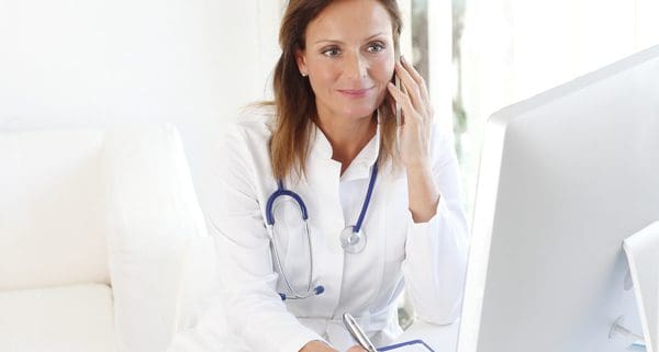 A female nurse wearing a stethoscope takes a call on a cellphone while in a medical office. 